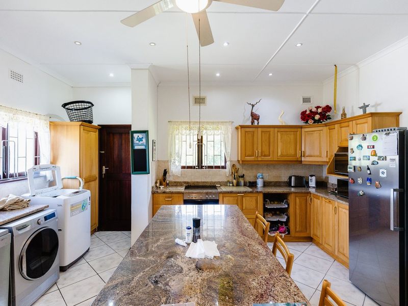 A functional kitchen featuring wooden cabinetry, granite countertops, a central island, and integrated laundry appliances, offering a practical layout for daily use.