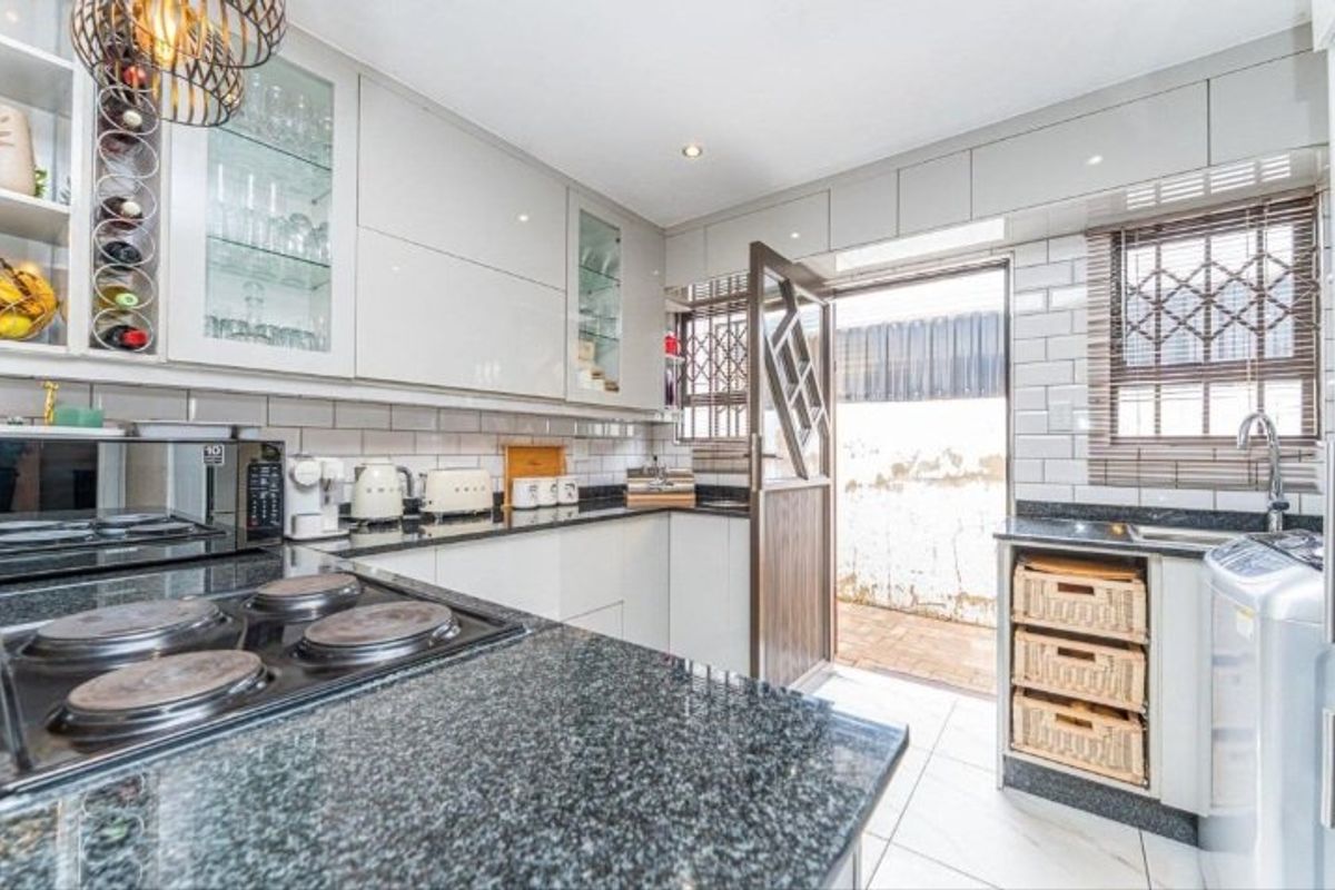 Modern kitchen featuring sleek cabinetry, granite countertops, subway tile backsplash, and direct access to an outdoor area through a secure door.