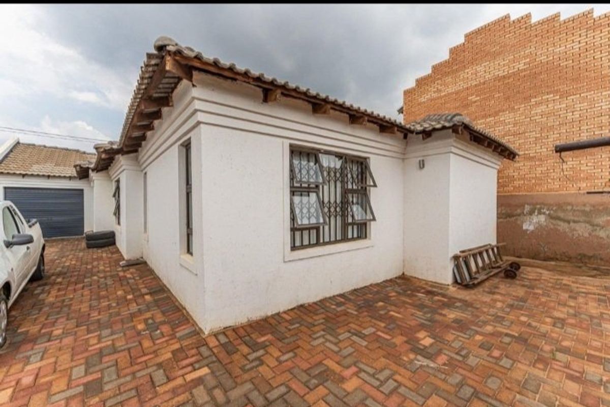 Rear exterior view of the house featuring paved driveway, tiled roof, and security-fitted windows, set against a brick boundary wall.