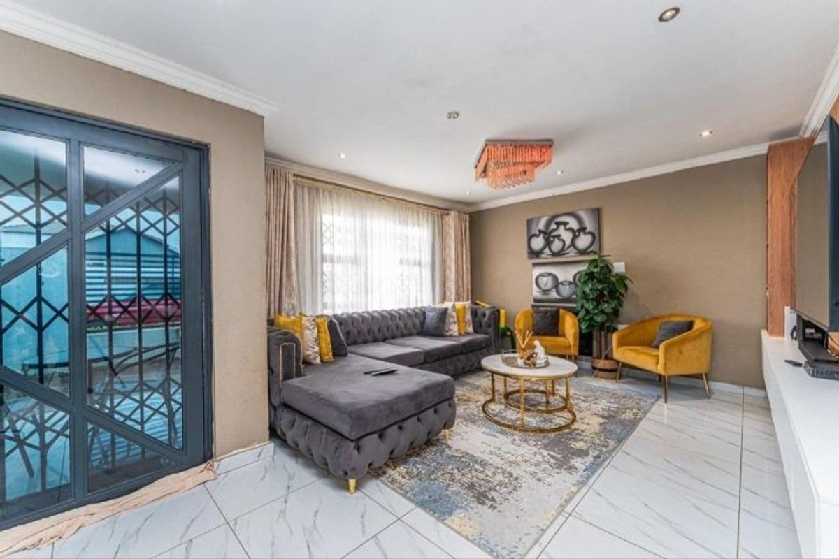A well-maintained living room featuring polished tiled flooring, recessed lighting, crown molding, and a built-in media unit with a secure entrance door.
