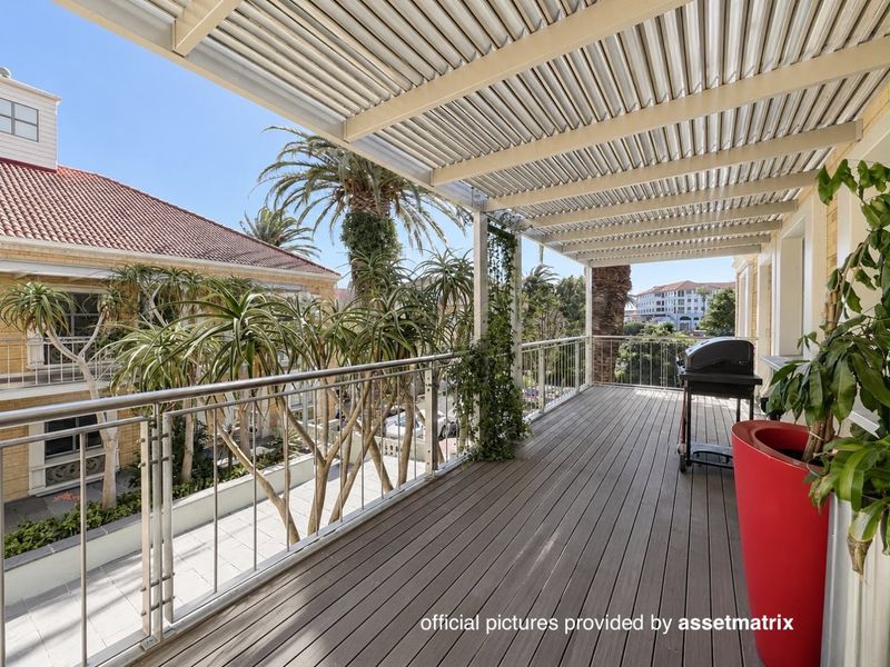 Spacious balcony featuring composite decking, a modern stainless steel balustrade, and a protective metal pergola, offering a pleasant outdoor area.