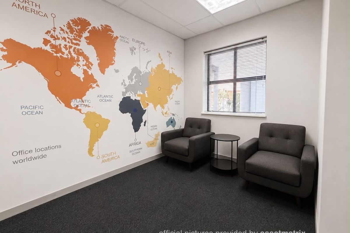 A professional office space featuring a world map wall graphic, carpeted flooring, and a window with venetian blinds.