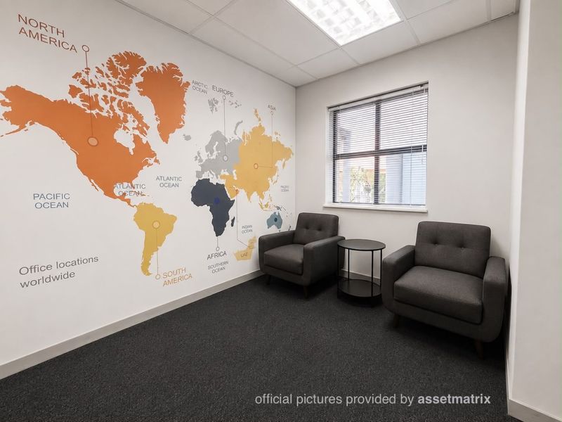 A professional office space featuring a world map wall graphic, carpeted flooring, and a window with venetian blinds.