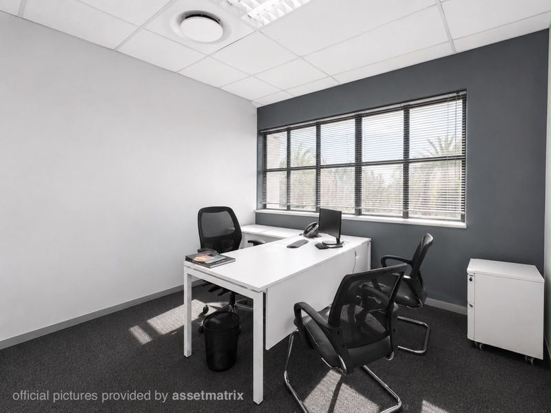 A professional office space featuring a suspended ceiling, recessed lighting, carpeted flooring, and large windows with venetian blinds.
