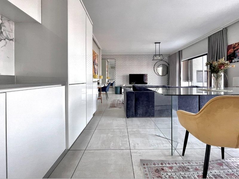 Modern open-plan living area featuring sleek white cabinetry, marble-look backsplash, large format floor tiles, and seamless flow to the outdoor balcony.