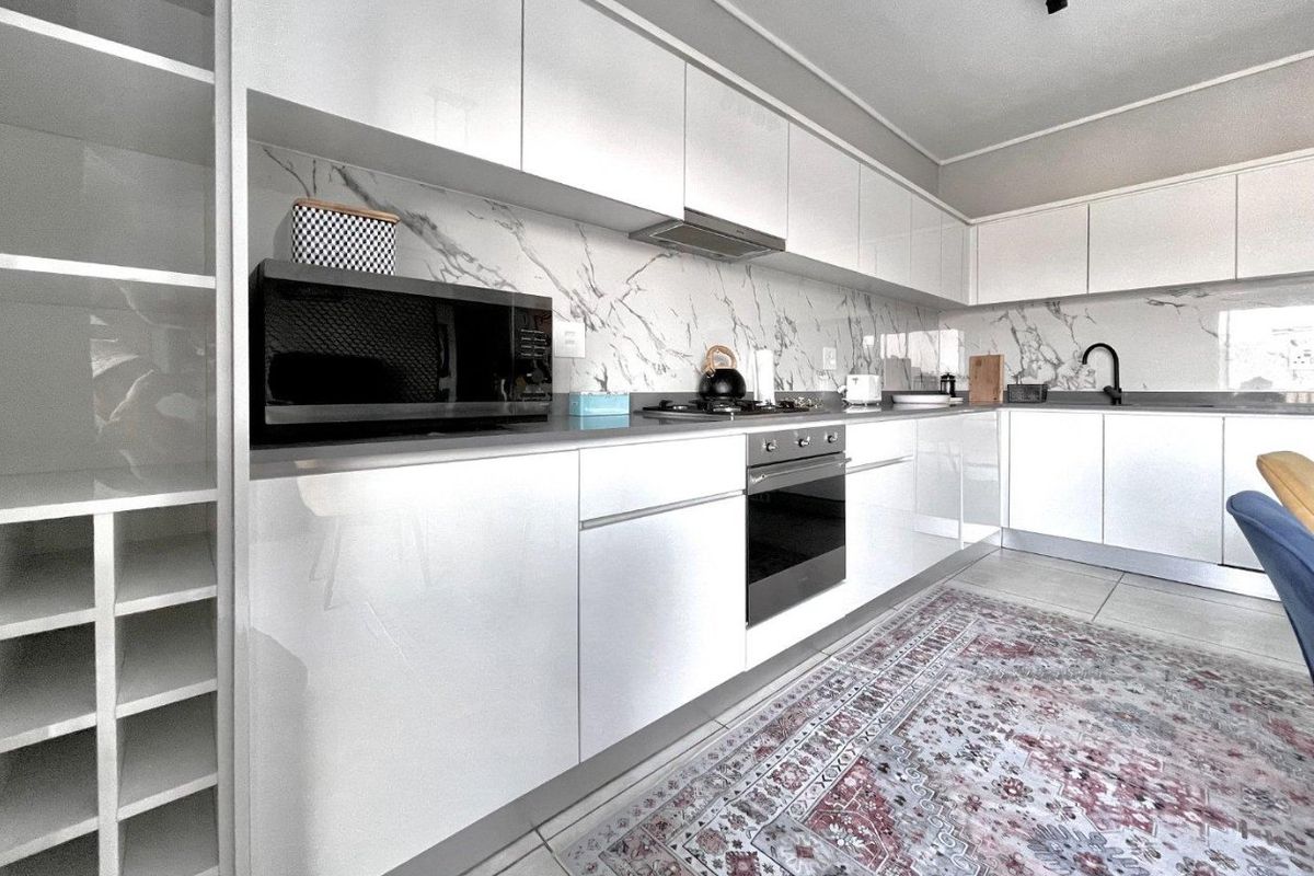 Modern kitchen featuring high-gloss white cabinetry, marble-look splashback, integrated oven, hob, extractor fan, and sleek undermount sink with contemporary finishes.