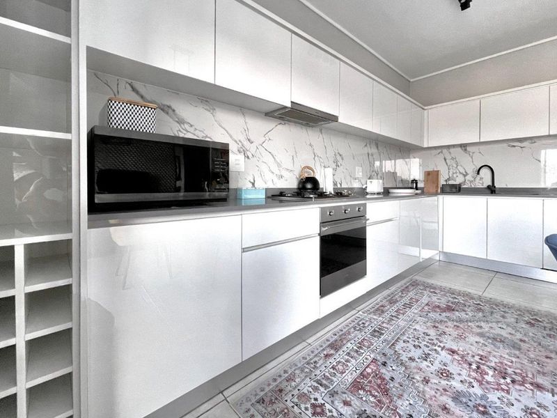 Modern kitchen featuring high-gloss white cabinetry, marble-look splashback, integrated oven, hob, extractor fan, and sleek undermount sink with contemporary finishes.