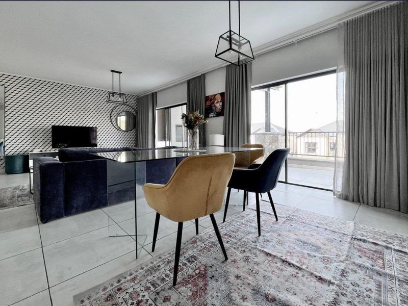 Spacious open-plan living and dining area featuring large format floor tiles, modern pendant lighting, and sliding glass doors leading to a balcony.
