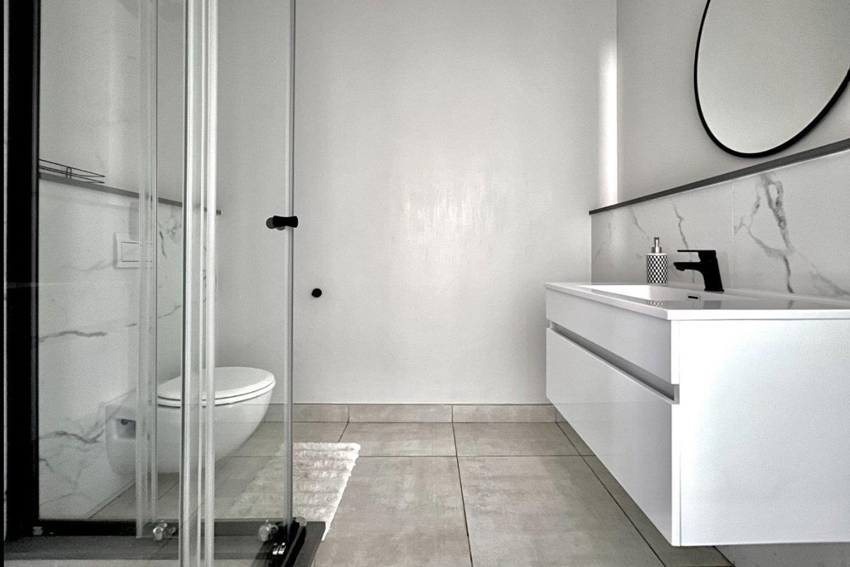 Modern bathroom featuring a wall-mounted vanity, wall-hung toilet, glass shower enclosure, and elegant marble-effect wall tiling with contemporary black fixtures.