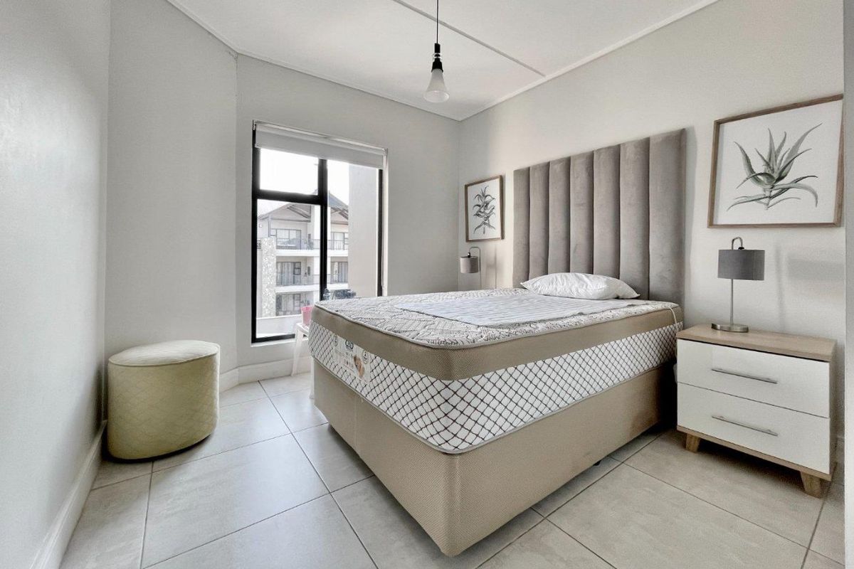 A bright and modern bedroom featuring neutral tiled flooring, a large window with a roller blind, and a contemporary pendant light fixture.