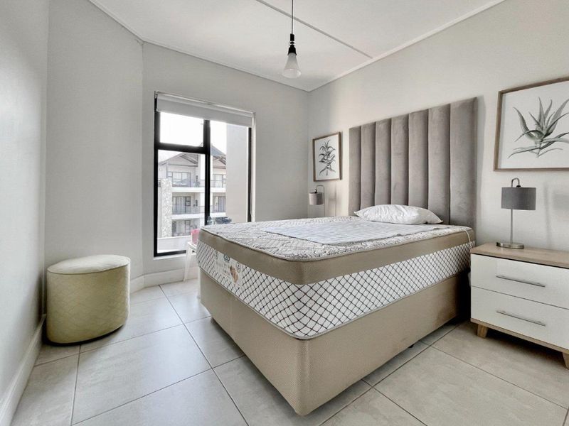 A bright and modern bedroom featuring neutral tiled flooring, a large window with a roller blind, and a contemporary pendant light fixture.