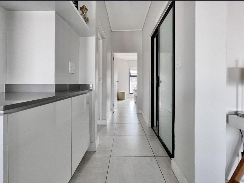 A bright, modern hallway featuring neutral tiled flooring, built-in cabinetry with stone countertops, and a sleek sliding glass door leading to adjacent rooms.