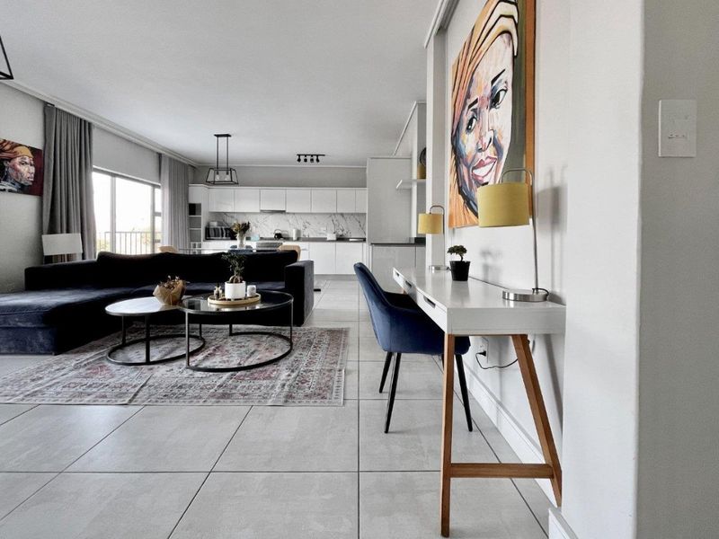 A modern open-plan living and kitchen area featuring sleek white cabinetry, marble-look backsplash, large format floor tiles, and access to a balcony.