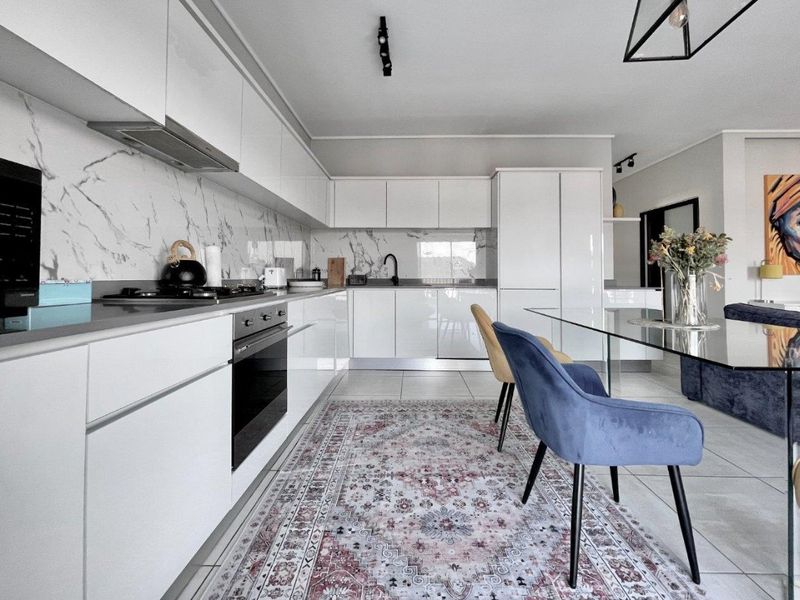 Modern open-plan kitchen featuring sleek white cabinetry, marble-look splashbacks, integrated appliances, and high-quality tiled flooring.