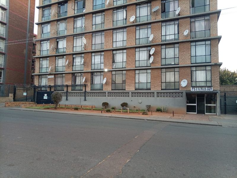 Street view of a multi-story brick apartment building featuring metal-framed windows and a ground-level security entrance.