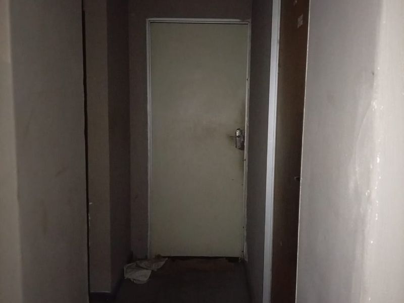A narrow, dimly lit interior hallway featuring plain walls and internal doors, requiring cosmetic updates to improve the overall aesthetic.