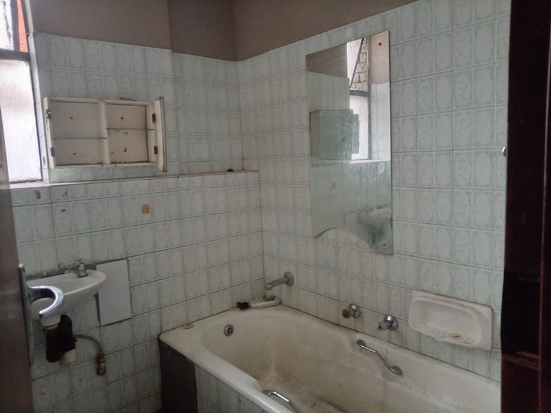 A dated bathroom featuring a bathtub, wall-mounted basin, and tiled walls, requiring significant renovation and modernization of fixtures and finishes.