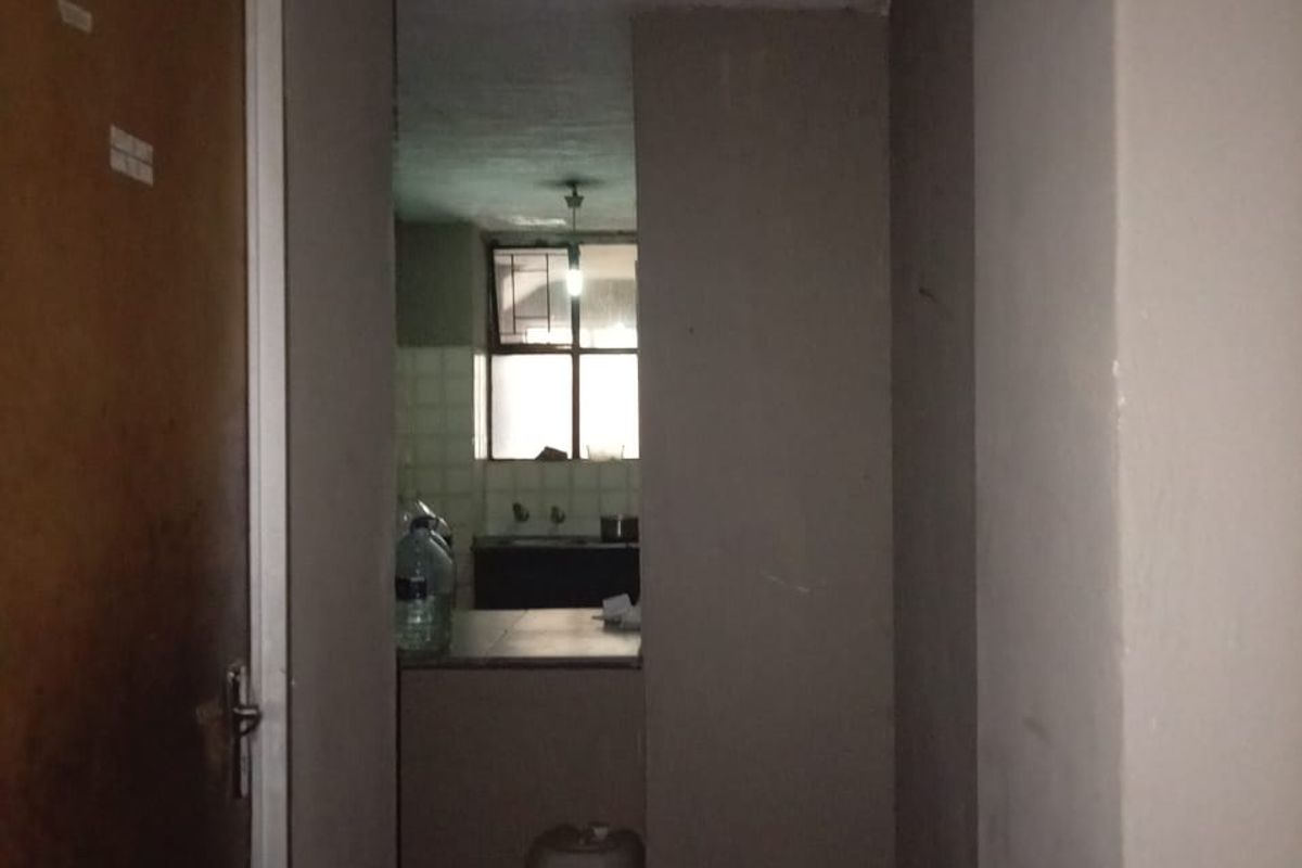 A dimly lit hallway leading into a kitchen area with basic cabinetry and sink fixtures.