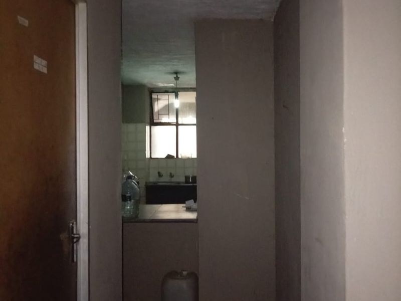 A dimly lit hallway leading into a kitchen area with basic cabinetry and sink fixtures.