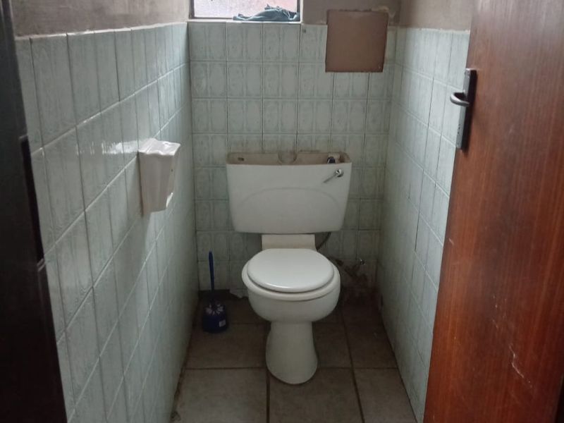 A small, dated bathroom featuring tiled walls and flooring, currently requiring maintenance and cosmetic updates to the fixtures and wall finishes.