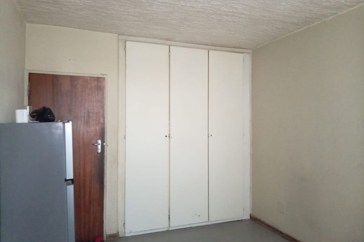 A vacant bedroom featuring built-in cupboards, a textured ceiling, and a timber door, requiring cosmetic updates to improve its overall condition.