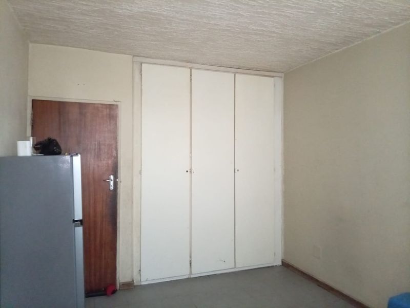 A vacant bedroom featuring built-in cupboards, a textured ceiling, and a timber door, requiring cosmetic updates to improve its overall condition.