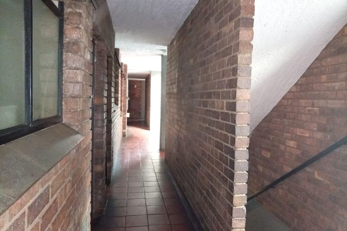 A narrow hallway featuring exposed brick walls and tiled flooring, leading towards an open stairwell area.