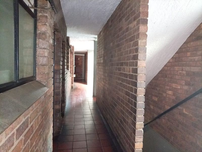 A narrow hallway featuring exposed brick walls and tiled flooring, leading towards an open stairwell area.