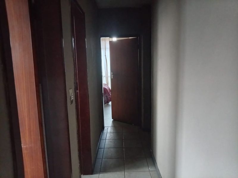 A narrow interior hallway featuring tiled flooring and wooden door frames leading to adjacent rooms.