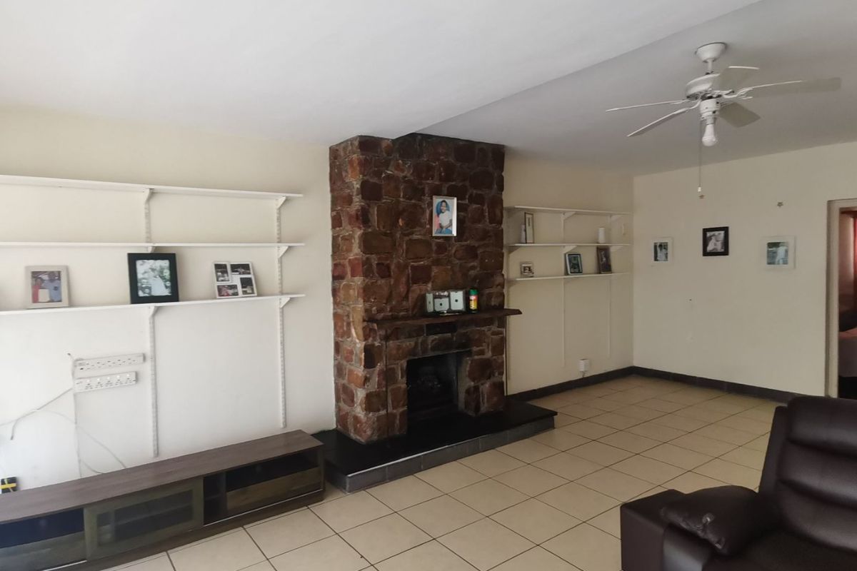 Spacious living room featuring a prominent stone fireplace, ceramic tiled flooring, ceiling fan, and built-in wall shelving.