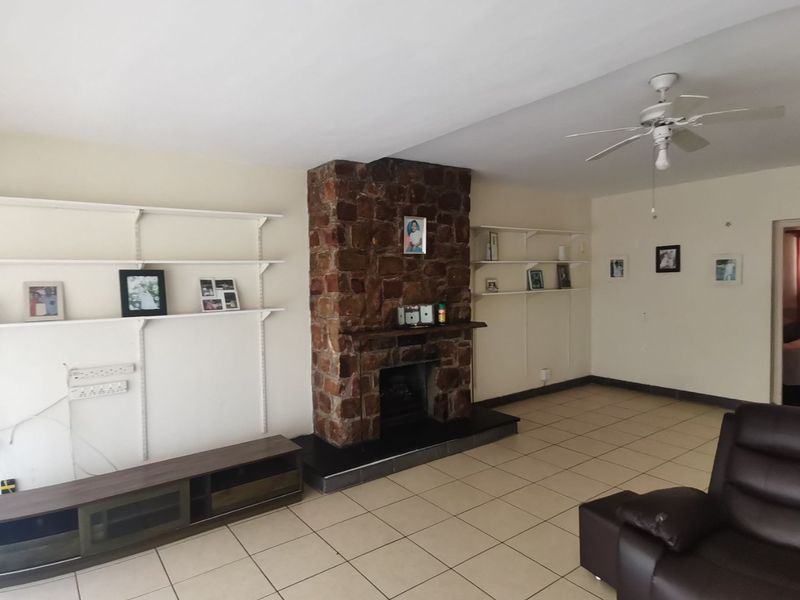 Spacious living room featuring a prominent stone fireplace, ceramic tiled flooring, ceiling fan, and built-in wall shelving.