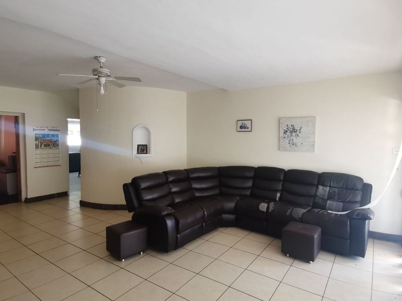 A spacious living area featuring neutral tiled flooring, a ceiling fan, and a decorative built-in wall niche.