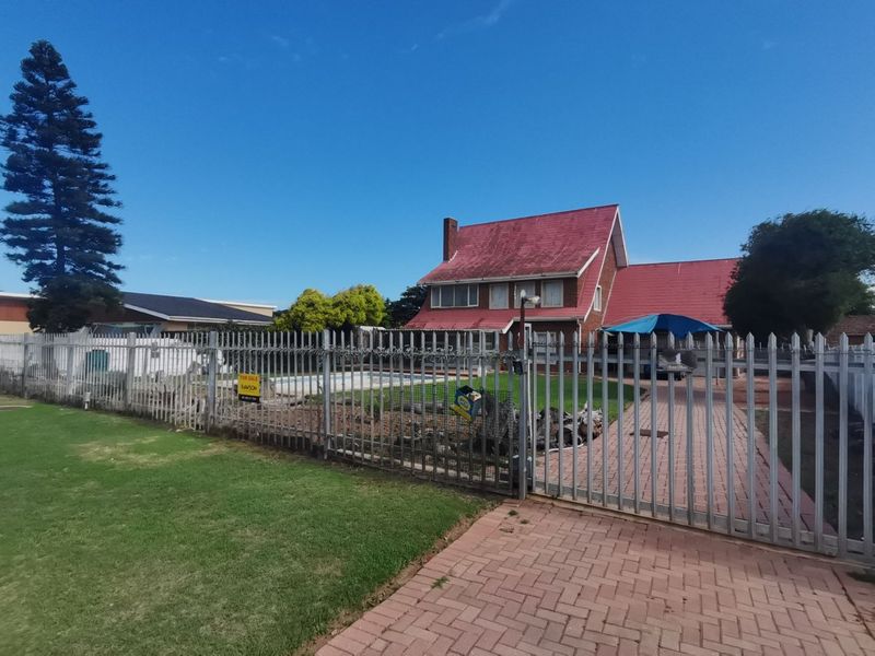 Front view of a residential property featuring a paved driveway, metal security fencing, and a swimming pool in the front garden area.