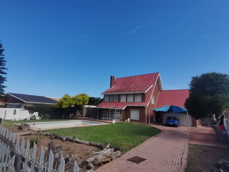 Rear view of a two-story brick house featuring a swimming pool, paved driveway, carport, and a large garden area.