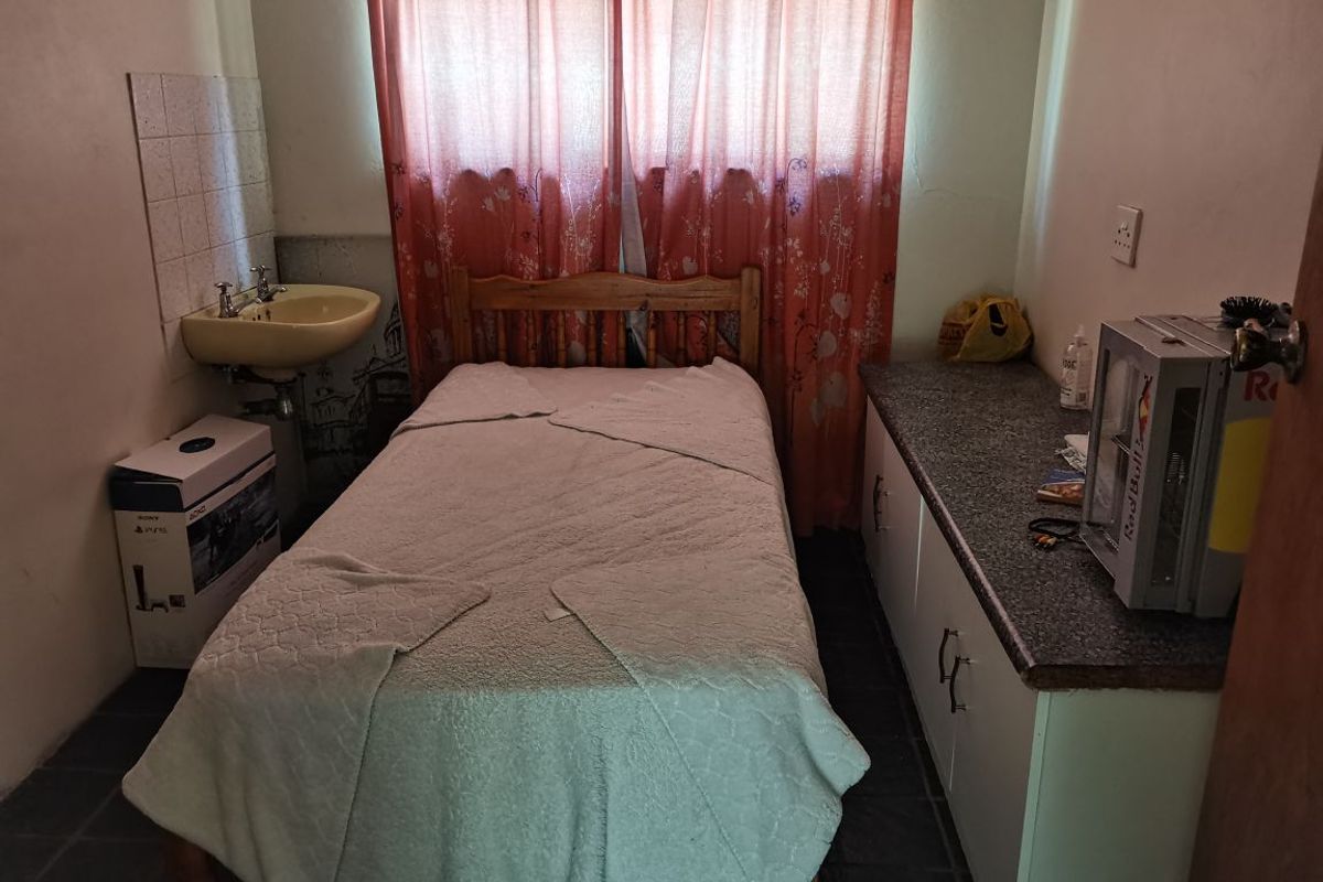 A compact bedroom featuring a built-in vanity with a basin, laminate countertop, and tiled flooring, offering potential for modernization.