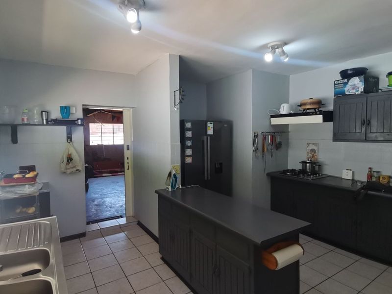 Functional kitchen featuring dark cabinetry, a central island, gas hob with extractor, and tiled flooring, with direct access to an adjacent utility area.