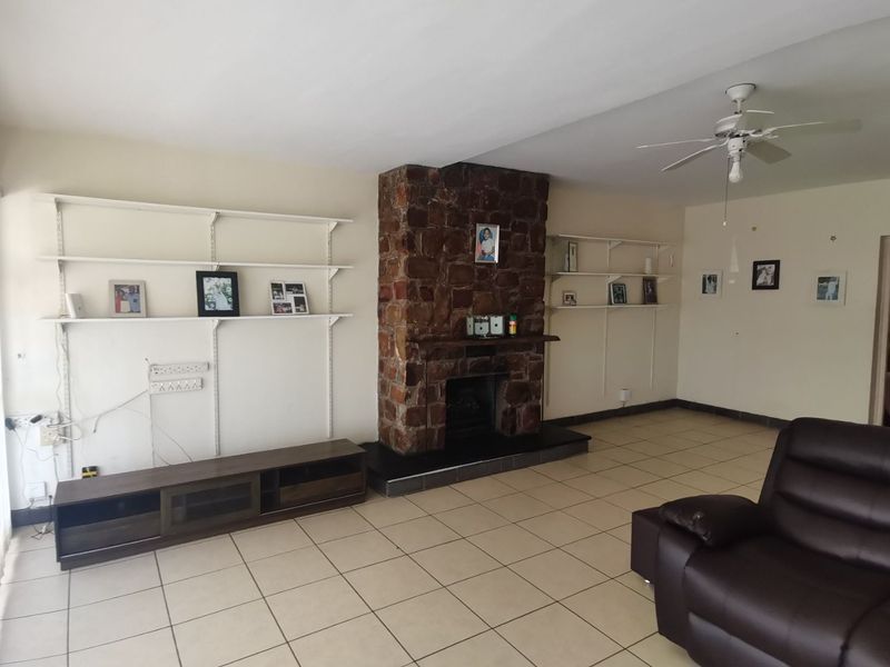 Spacious living room featuring a prominent stone fireplace, tiled flooring, ceiling fan, and built-in wall shelving units.