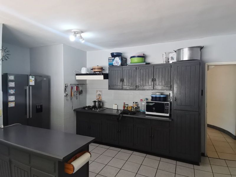 A functional kitchen featuring dark-painted built-in cabinetry, a gas hob with extractor fan, tiled backsplash, and a central kitchen island with tiled flooring.