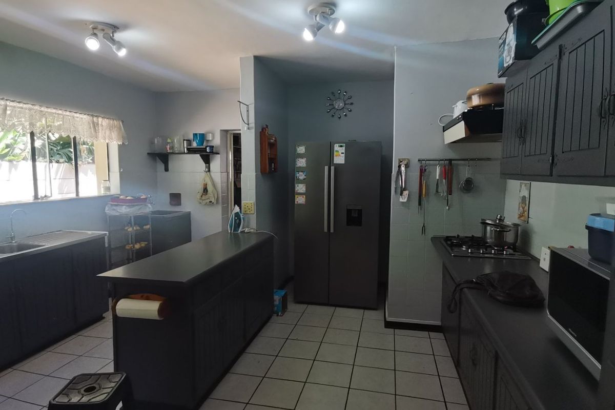 A functional kitchen featuring dark cabinetry, a central island, gas hob, extractor fan, and tiled flooring with ample counter space.