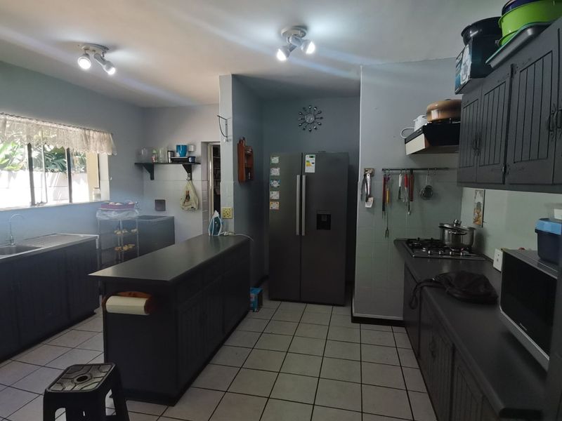 A functional kitchen featuring dark cabinetry, a central island, gas hob, extractor fan, and tiled flooring with ample counter space.