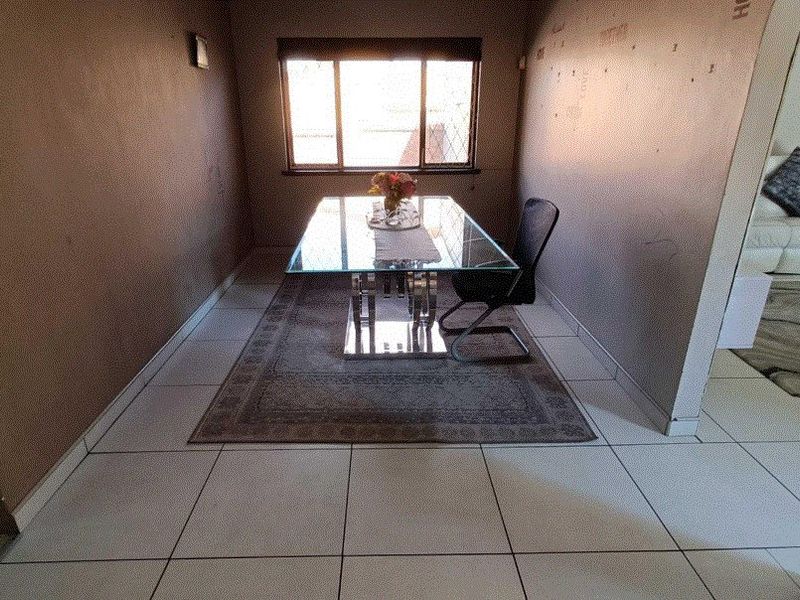 A dining room featuring tiled flooring and a window, currently showing signs of wear on the wall surfaces.
