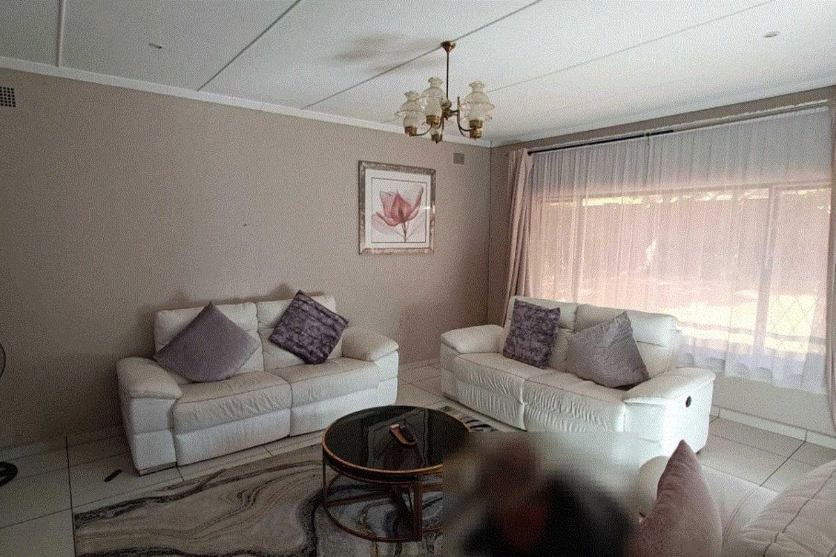 A comfortable living room featuring tiled flooring, neutral wall tones, and large windows with curtain treatments, providing a bright and functional space.