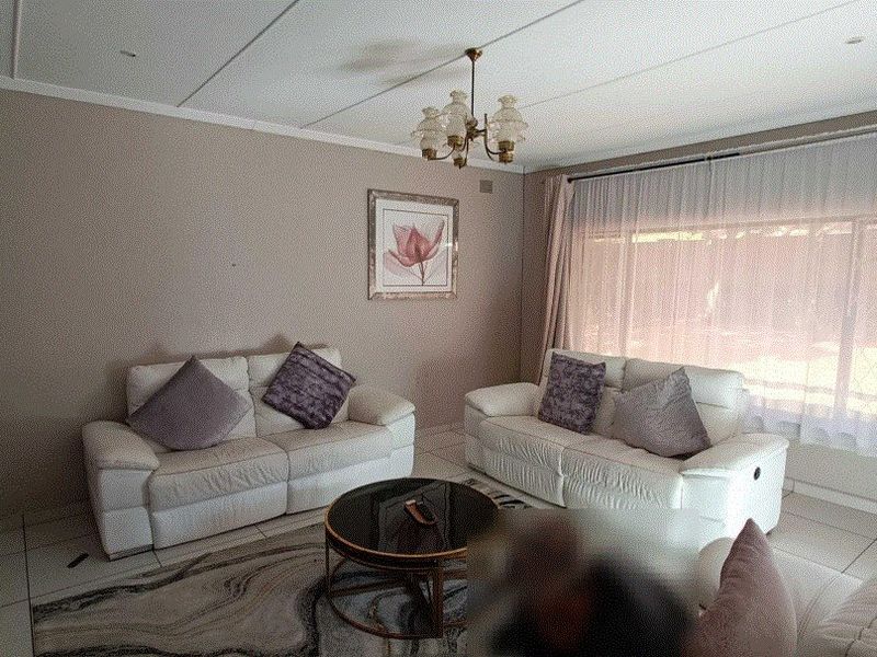 A comfortable living room featuring tiled flooring, neutral wall tones, and large windows with curtain treatments, providing a bright and functional space.