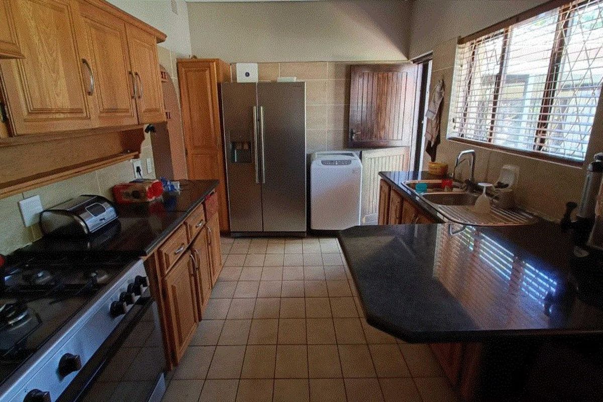 A functional kitchen featuring wooden cabinetry, granite countertops, a gas stove, and tiled flooring with direct access to an outdoor area.