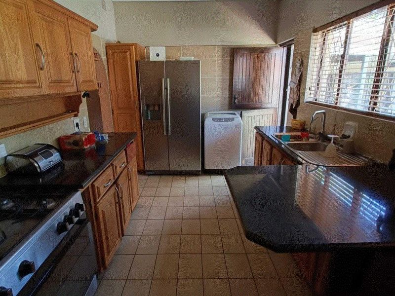 A functional kitchen featuring wooden cabinetry, granite countertops, a gas stove, and tiled flooring with direct access to an outdoor area.