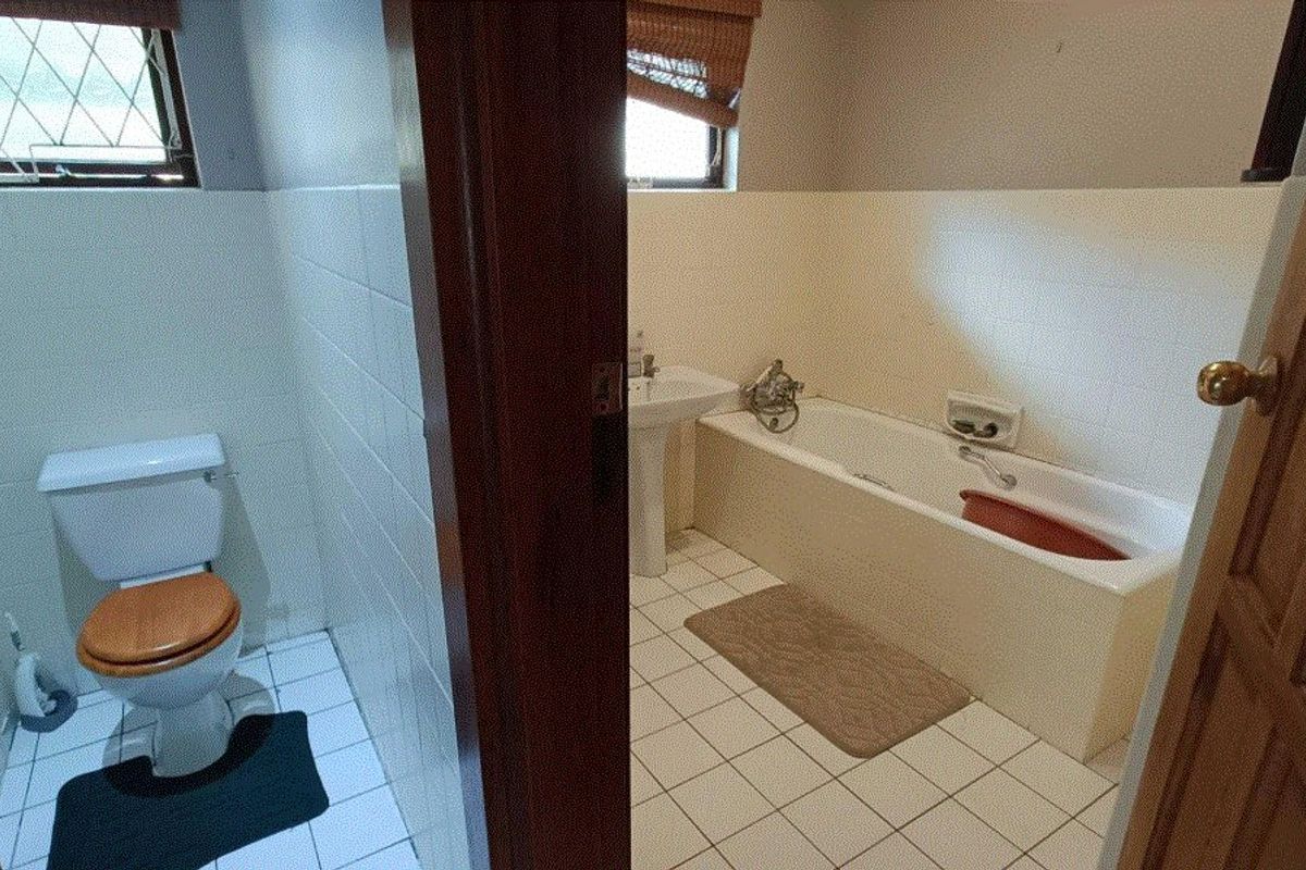 A dated bathroom featuring a standard bathtub, pedestal basin, and toilet with tiled flooring and walls.