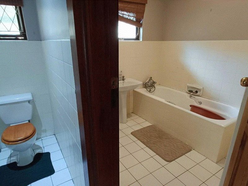 A dated bathroom featuring a standard bathtub, pedestal basin, and toilet with tiled flooring and walls.