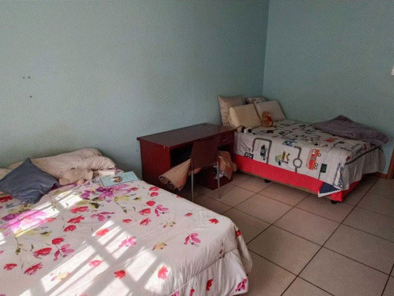 A bedroom featuring tiled flooring and light blue walls, currently configured with two beds and a desk.