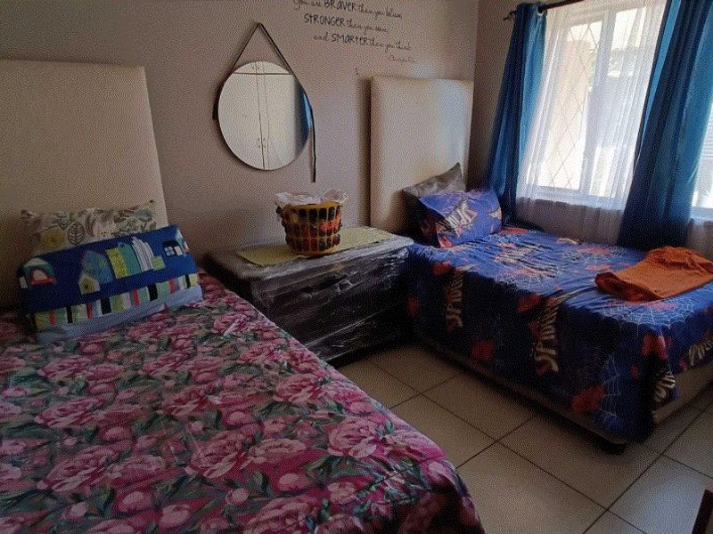 A functional bedroom featuring tiled flooring and a window with security bars, providing a practical space for sleeping or study.