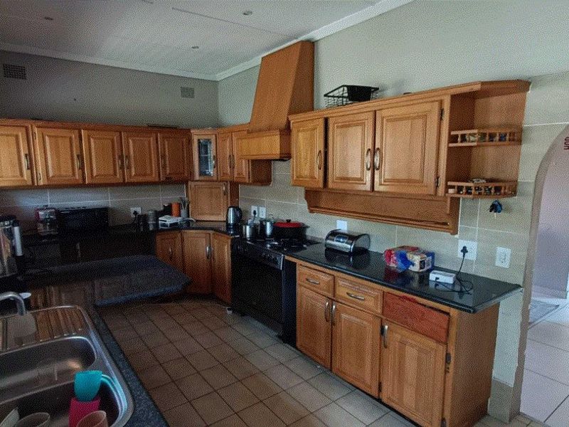 A functional kitchen featuring wooden cabinetry, granite countertops, a double stainless steel sink, and a built-in extractor hood with tiled flooring and backsplash.